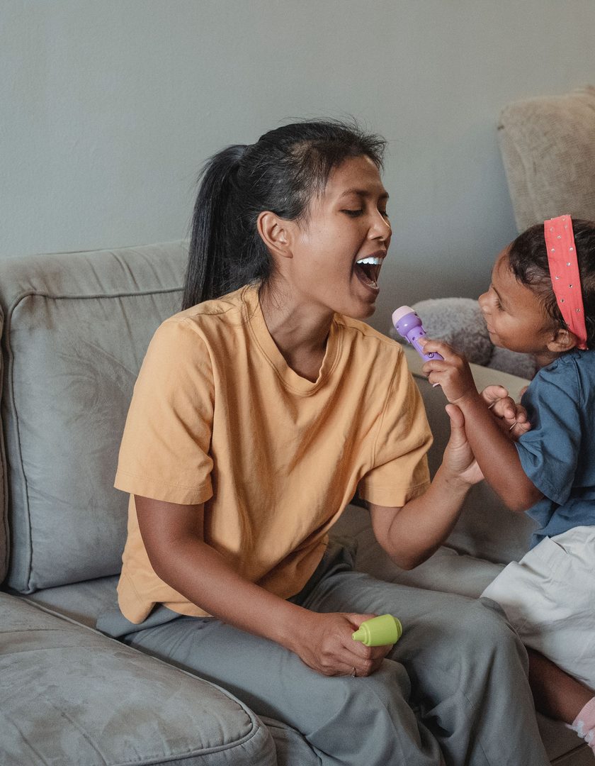 A carer and a young girl playing together on a sofa at home